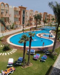 a large swimming pool with chairs and palm trees at Résidence les dunes in Hammam Sousse