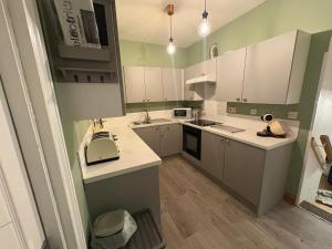 a small kitchen with white cabinets and green walls at Seaton, Devon, two bed apartment, just off the sea front. in Seaton