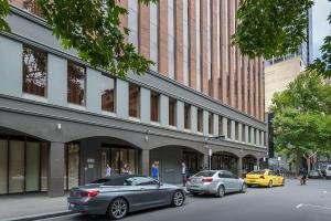 deux voitures garées dans une rue en face d'un bâtiment dans l'établissement Mantra on Little Bourke, à Melbourne