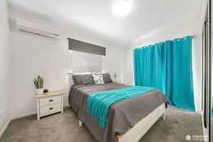 een slaapkamer met een bed en een raam met blauwe gordijnen bij Air-conditioned Cooee Bay Beach House with Wi-Fi in Yeppoon