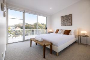 a white bedroom with a bed and a balcony at Luxurious Waterfront Retreat in Oatley in Oatley