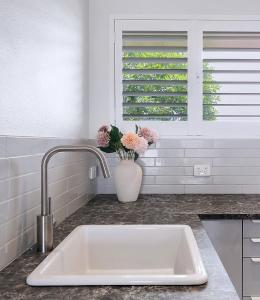 a white sink in a kitchen with a vase of flowers at Greenslopes Cityview Haven in Brisbane