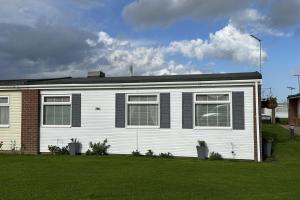 ein weißes Haus mit schwarzen Fenstern und einem Rasenplatz in der Unterkunft Dog friendly chalet in Hemsby by Winterton Cottages in Hemsby