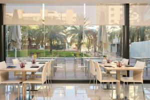 バルセロナにあるCatalonia Barcelona Beachのテーブルと椅子と大きな窓のあるレストラン