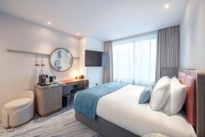 a hotel room with a bed and a desk at Dorsett Hotel Canary Wharf in London +4 photos