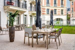 un patio con tavolo, sedie e ombrelloni di Zenao Appart'hôtels Le Raincy Thiers a Le Raincy