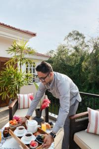 a man standing on a balcony with a tray of food at LohonoStays Calisto Villa C in Siolim