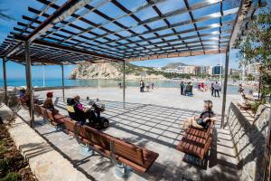 a group of people sitting on benches near the beach at Apartamento Elegance La Cala Benidorm in Benidorm