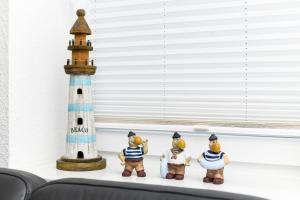 een groep beeldjes zittend op een plank naast een vuurtoren bij Ferienhaus Lüttje Krabbe in Carolinensiel