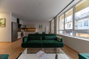 a living room with a green couch and a kitchen at L'Hotel des Postes - Appartement design en centre ville in Vichy