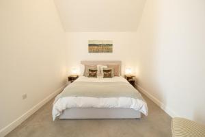 a white bedroom with a bed and two lamps at Eastcombe Barn in Castle Combe