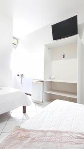 a white bedroom with two beds and a tv at Pousada Central in Feira de Santana