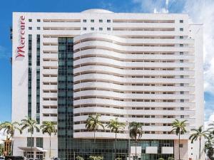 a large white building with palm trees in front of it at Flat moderno Hotel Mercure Líder in Brasilia