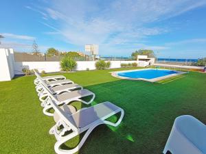 a row of lounge chairs on a lawn with a pool at MILÚ GOLF LUXURY HOUSE in Caleta De Fuste