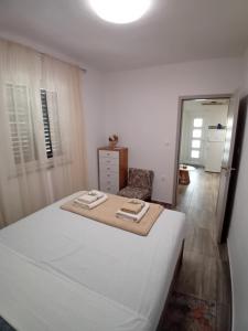 a white bedroom with a bed and a chair at Apartmani Vrzić in Baška