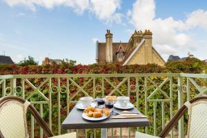 a table with a plate of food on a balcony with a castle at La Closerie SPA & Résidence Hôtel in Deauville