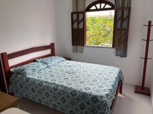 a bedroom with a bed with a blue comforter and a window at Casa da Ilha de Boipeba in Ilha de Boipeba