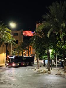 Luxury Apartments Near the Beach and Downtown CENTRUM 8 في أليكانتي: حافلة تنزل على شارع فيه نخيل بالليل