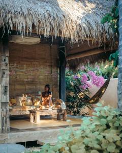 una mujer sentada en una cama en una cabaña de paja en Gili Asahan Eco Lodge & Restaurant, en Gili Asahan