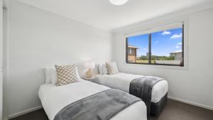 a white bedroom with two beds and a window at Brunswick Beach Club - Coastal Comfort Near Beach in Coffs Harbour +15 photos