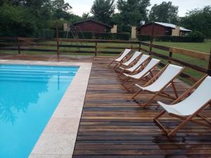 una fila de sillas sentadas en una terraza de madera junto a una piscina en Posta Mágica en Los Reartes