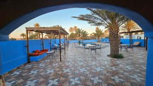 a patio with tables and chairs and a palm tree at Auberge Les Roches in Merzouga