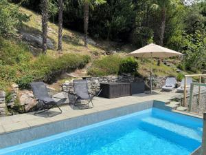 a swimming pool with two chairs and an umbrella at Casa Girasol by Fewotessin in Cavigliano