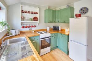 a kitchen with green cabinets and a white refrigerator at Traditional cottage with brand new Woodburner in Wark