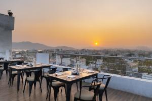 ein Restaurant mit Tischen und Stühlen auf einem Balkon mit Blick auf den Sonnenuntergang in der Unterkunft Amoraya Udaipur in Udaipur