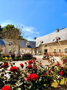 un gran edificio con rosas rojas delante de él en Chambres Résidentielles avec cuisine au Manoir de Mathan à Crépon 5 mn D'Arromanches et 10 mn de Bayeux, en Crépon