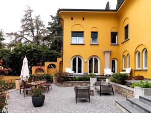 a yellow building with chairs and tables and a umbrella at Villa Ella con Depandance in Gardone Riviera