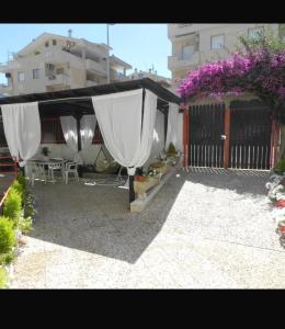 a patio with a white canopy and tables and purple flowers at Chira House in Santa Marinella