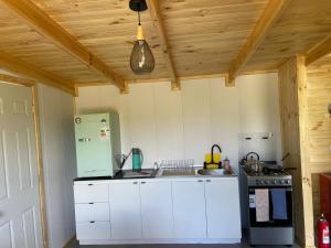 Una cocina con gabinetes blancos y un electrodoméstico verde. en Cabañas Aurora, en Quilquico
