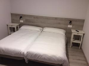 uma cama grande com lençóis brancos e duas mesas em La Casa de los Soportales em Mansilla de las Mulas