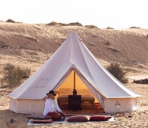 a woman sitting in front of a white tent in the desert at Bidiyah Old Bedouin Wahaiba Desert CAMP in Badīyah