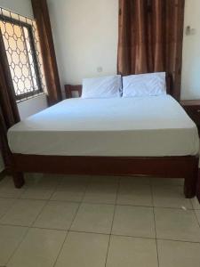 Una cama con sábanas blancas y almohadas en una habitación. en Home away from home, en Moshi