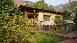 una casa con sedie e ombrellone in cortile di The Countryside Cottage in Mulshi a Mulshi