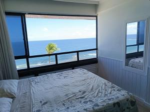 a bedroom with a view of the ocean from a window at Farol Barra Flat in Salvador