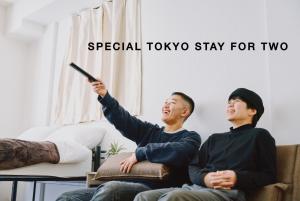 two men sitting on a couch looking at a remote control at Evergreen Apartment Hotel in Tokyo