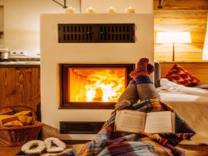 a person laying on a bed reading a book in front of a fireplace at Ferienhaus in Schierke mit Garten in Schierke