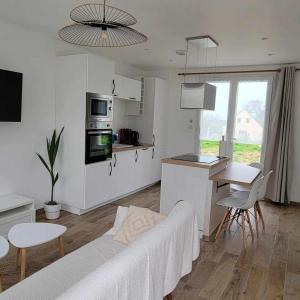 a white living room with a couch and a kitchen at petite maison 3km de la mer in Ozeville