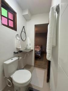 a bathroom with a toilet and a window and a bed at Casa da Pri Suítes in Pôrto de Pedras