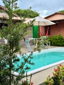 a pool with an umbrella and a table and chairs at Casa 02 na villa uryah in Caraíva