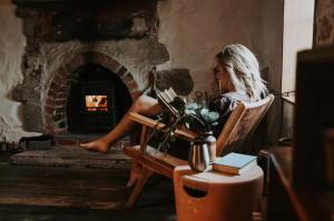 a woman sitting in a chair in front of a fireplace at Simplistic Luxury Cottage, Ross in Ross