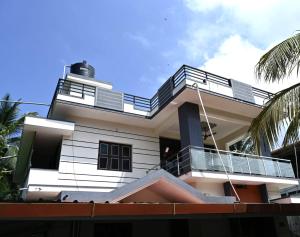 a white house with a balcony and palm trees at Providence homestay malpe in Udupi