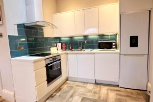 a kitchen with white cabinets and a sink and a refrigerator at The Hideaway With AC in London
