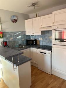Una cocina con gabinetes blancos y encimeras negras. en Appartement proche mer, en Bray-Dunes