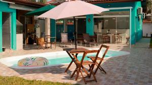 une table et des chaises avec un parasol à côté d'une piscine dans l'établissement Casa de Praia em Bertioga, São Paulocom Piscina Ar Condicionado Wifi a 500m do Mar, à Bertioga