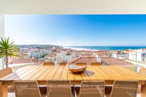 a wooden table with chairs and a view of the ocean at Villa Surf Vista - Praia da Areia Branca in Lourinhã