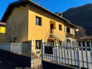 a yellow house with a white fence in front of it at Petra House in Porlezza